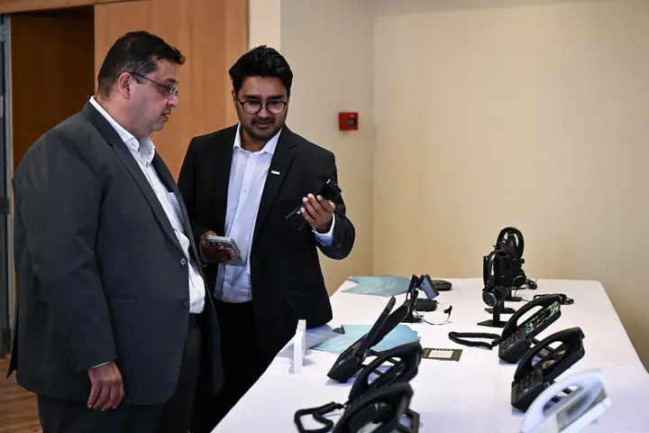 Two attendees looking at Snom desk phones and handsets on a display table